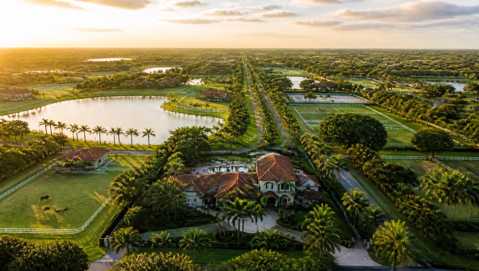 Aerial view of Wellington, Florida equestrian estates, white-fenced paddocks and lakes at golden hour